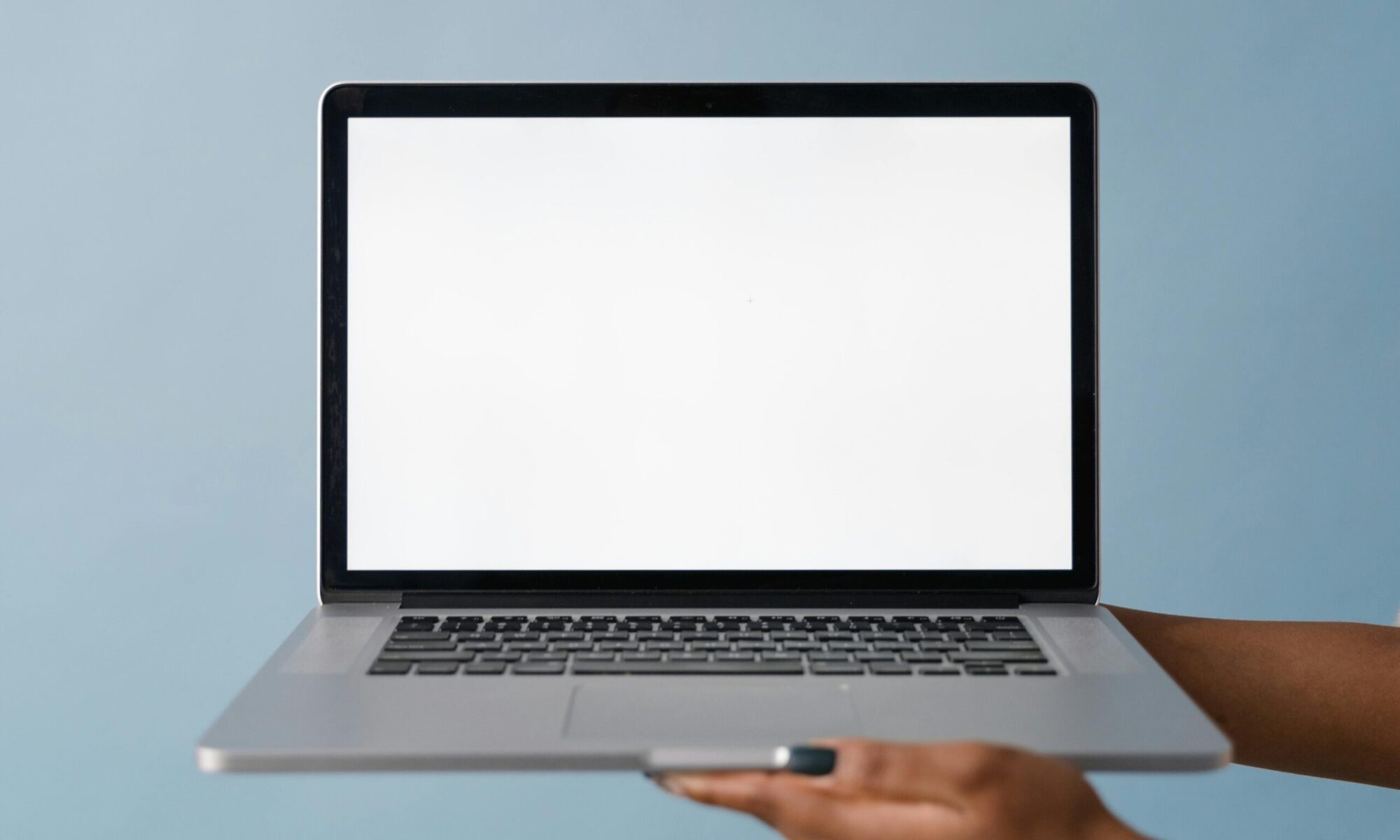 Person holding a rental lightweight laptop with blank screen on blue background.